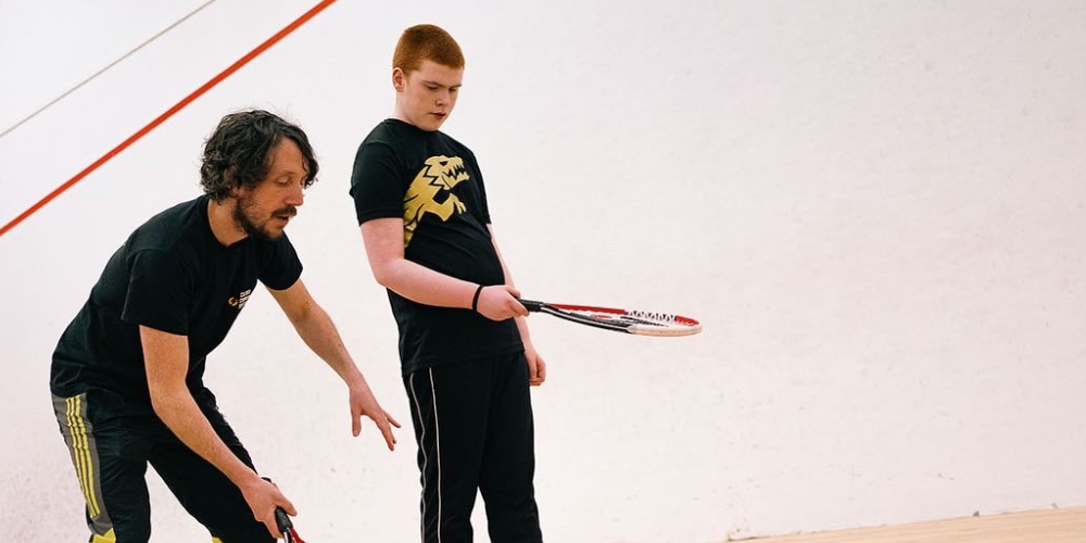 male coach teaching young man how to play squash on a squash court